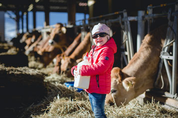 Kind mit voller Milchkanne, Kühe im Hintergrund am Biobauernhof Michlbauer